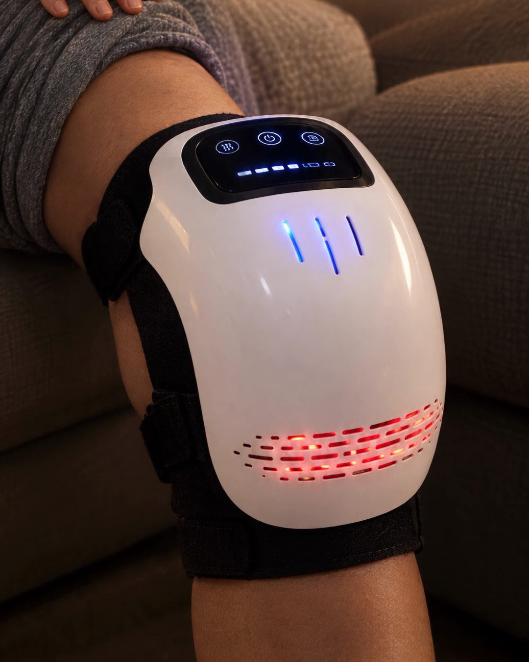 Close-up of the Noomo Knee Massager on a knee, switched on: touch panel lit, warm glow through the lower vents